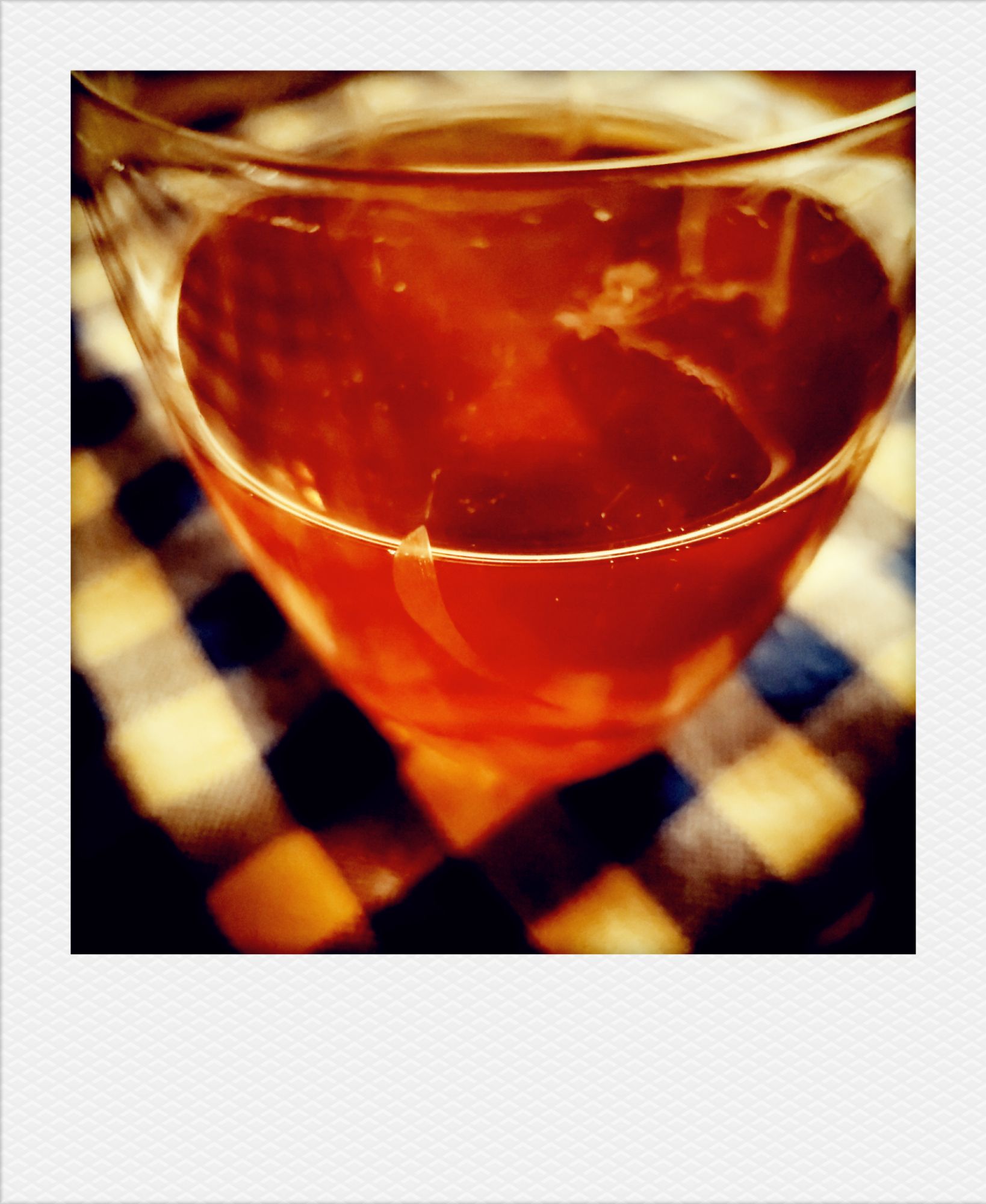 A small glass containing beer, on a squared tablecloth.