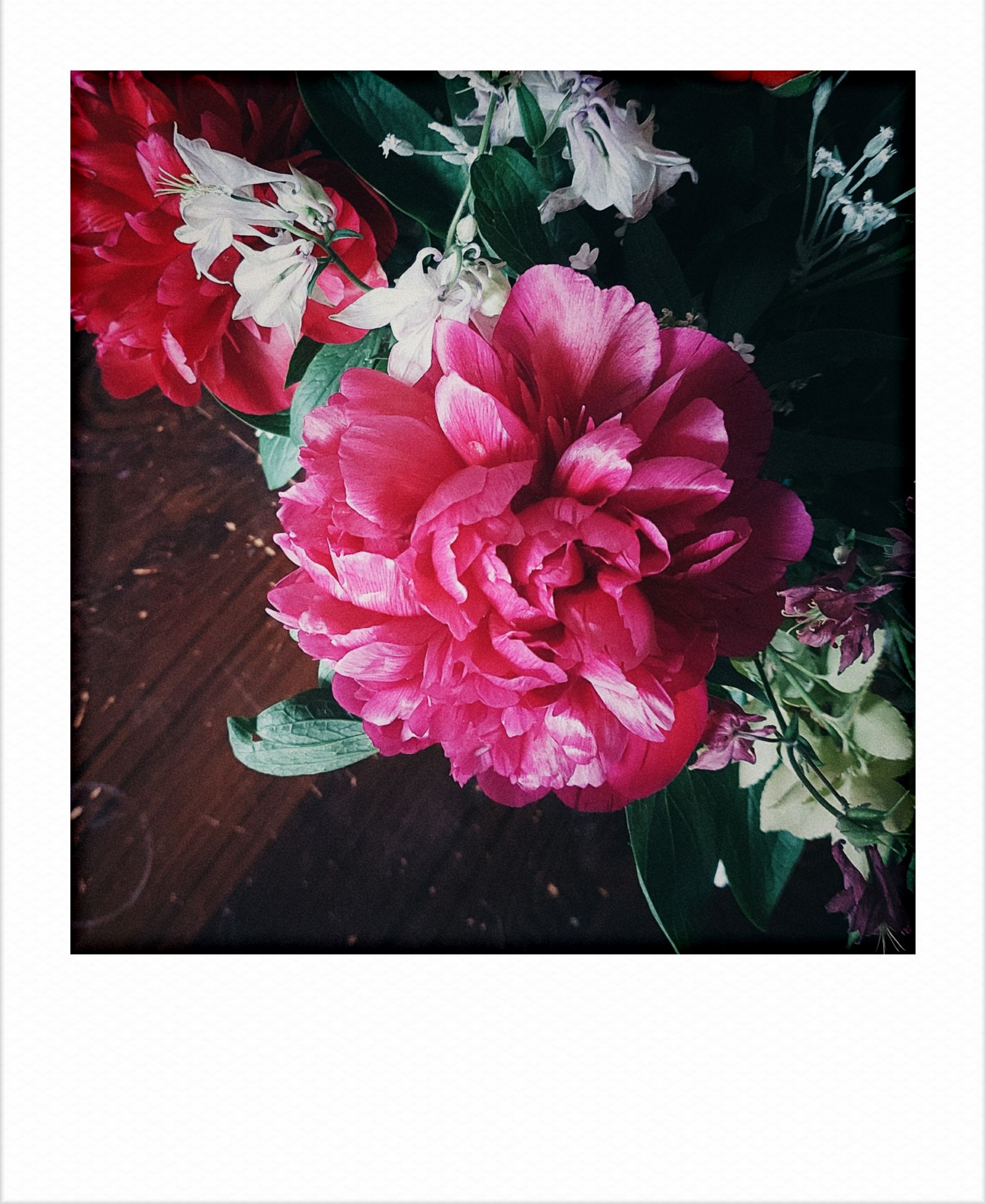 A bouquet of flowers with a very dominant peony on a dark wooden table.
