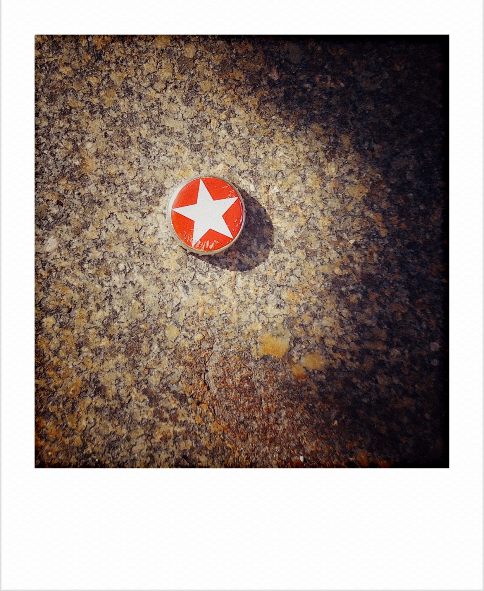 A bottle cap on a sidewalk. White star in a red filled circle.