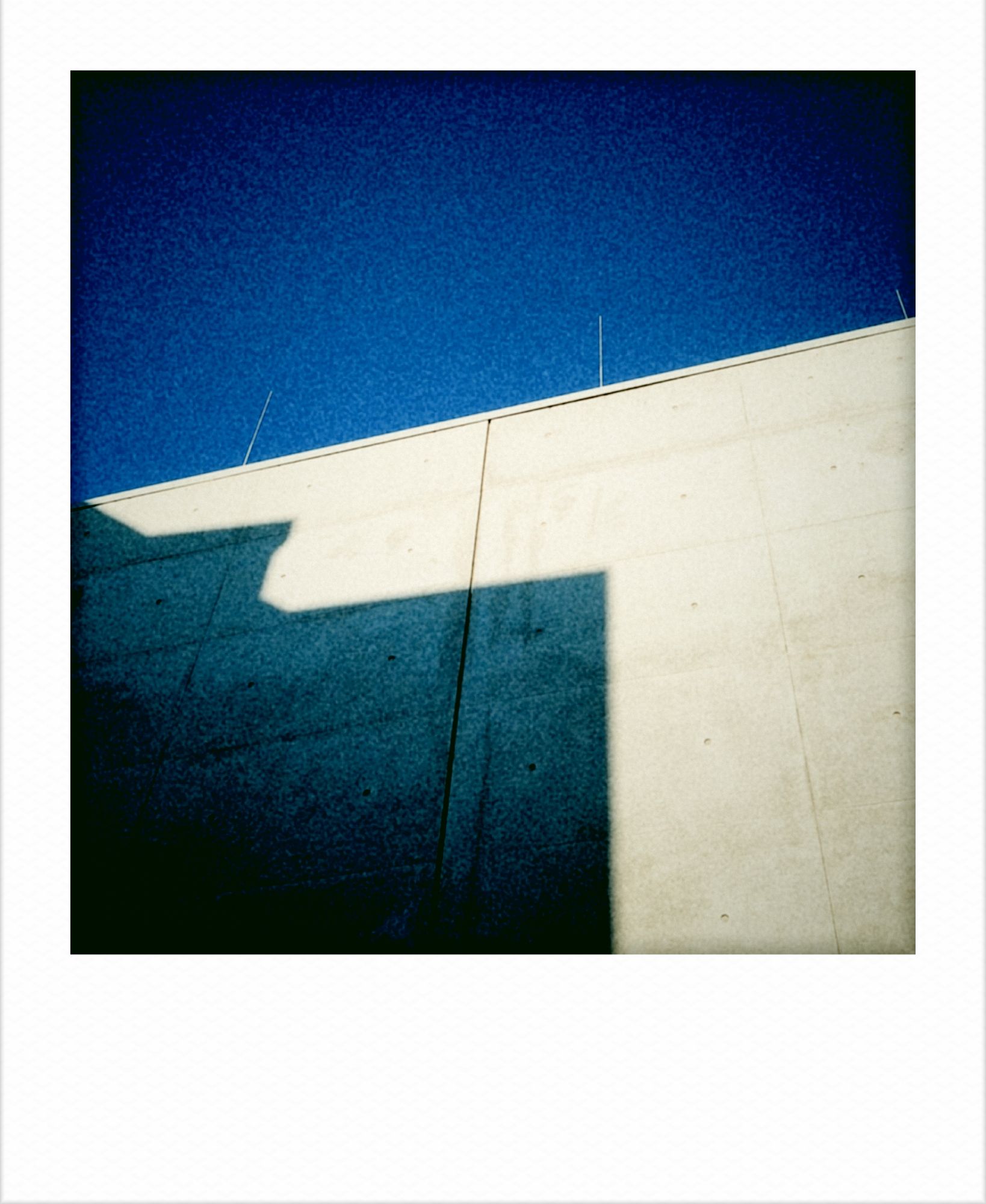 Building shadows on a concrete wall. Blue sky above.