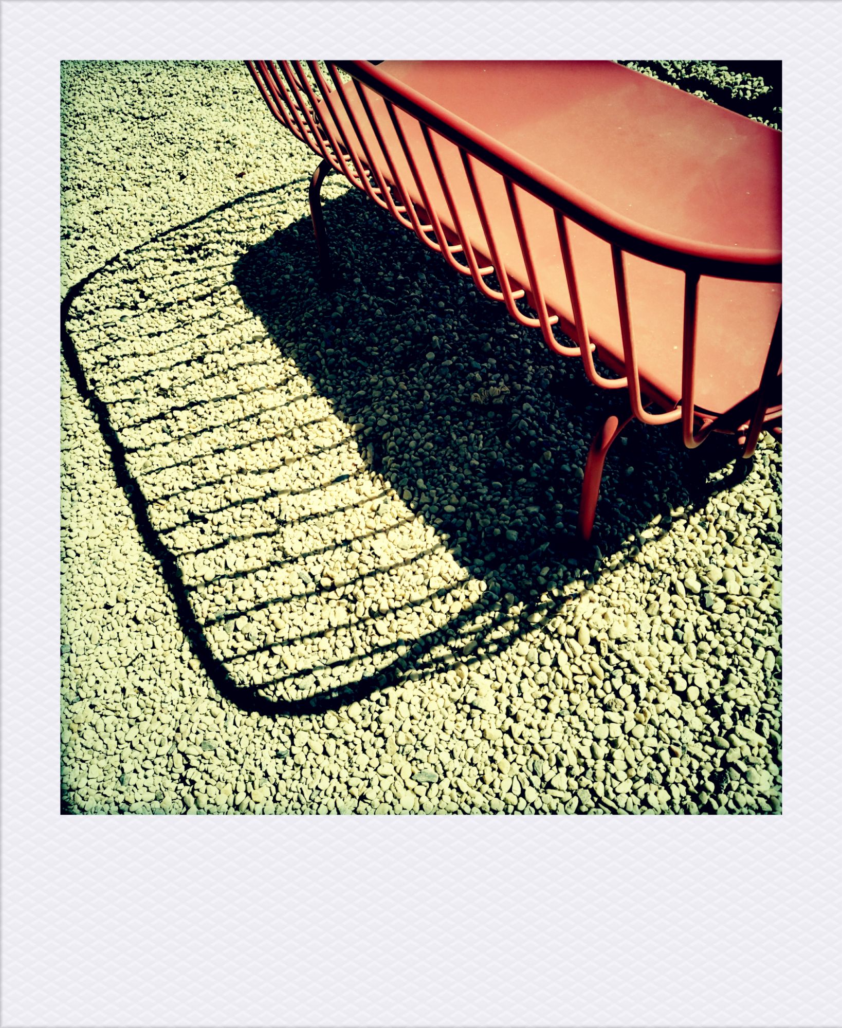An iron bench casting shadows on a grainy floor.